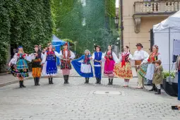 Grupa osób w tradycyjnych strojach ludowych tańcząca na ulicy.