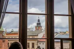 Widok na wieżę zegarową z okna, chmury na niebie.