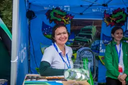 Kobieta w białej koszulce uśmiecha się przy stoisku z zielonymi akcentami.