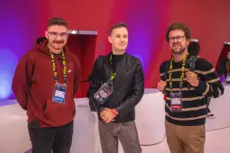 Trzech mężczyzn w casualowych ubraniach, stojących w nowoczesnym wnętrzu z kolorowym tłem.