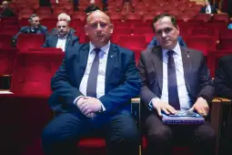 Dwaj mężczyźni siedzący na czerwonych fotelach w sali.