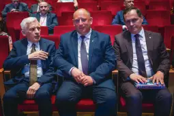 Trzech mężczyzn siedzących w czerwonych fotelach w sali konferencyjnej.