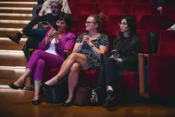 Trzy kobiety siedzące na czerwonych fotelach w sali konferencyjnej.