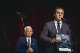 Mężczyzna w garniturze trzyma nagrodę, obok stoi starszy mężczyzna w garniturze.