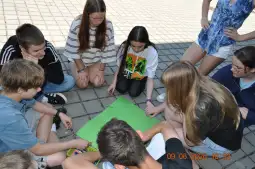 Grupa dzieci i młodzieży siedzi na ziemi, pracując nad projektem artystycznym.