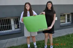 Dwie dziewczyny trzymają zielony plakat przed budynkiem.