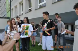 Grupa młodzieży na zewnątrz, rozmawiająca i trzymająca różne przedmioty.