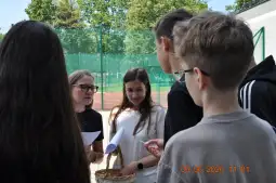 Grupa osób rozmawia na świeżym powietrzu, jedna z nich trzyma koszyk.