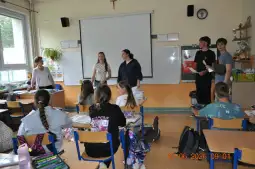 Uczniowie w klasie podczas prezentacji, nauczycielka obserwuje.
