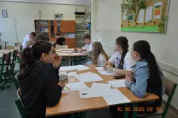 Grupa uczniów siedzi przy stole w klasie, pracując nad zadaniami.
