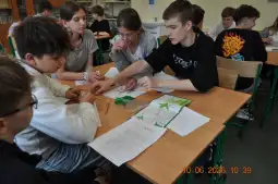 Grupa uczniów pracuje nad projektem w klasie, otoczeni materiałami edukacyjnymi.