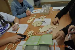 Grupa osób pracuje nad projektem z wykorzystaniem drewnianych elementów i instrukcji.