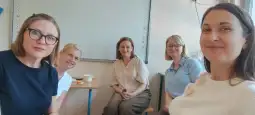 Grupa pięciu kobiet w biurze, uśmiechnięte, siedzą przy stole.