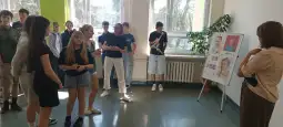 Grupa uczniów słuchających prezentacji przy tablicy z rysunkami.