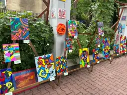 Wystawa kolorowych obrazów w stylu abstrakcyjnym na zewnątrz, otoczona zielenią.