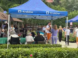Impreza plenerowa w Krakowie z uczestnikami przy stołach i namiotami.