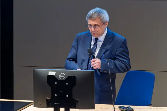Mężczyzna w garniturze przemawia do mikrofonu przy komputerze.
