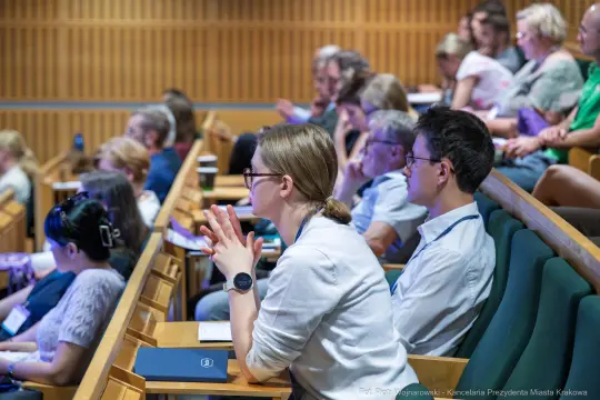 Grupa ludzi uczestniczących w konferencji, skupionych na prelekcji.