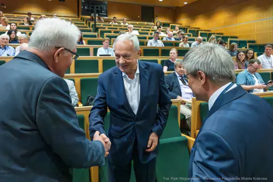 Spotkanie w sali konferencyjnej, mężczyźni witają się i rozmawiają. W tle uczestnicy wydarzenia.