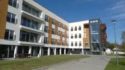 Nowoczesny budynek mieszkalny z dużymi oknami i zielonym otoczeniem.