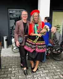 Dwie kobiety w tradycyjnych strojach ludowych, jedna z bukietem kwiatów.
