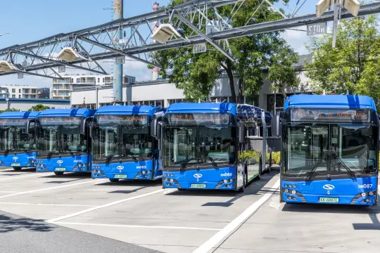 Pięć niebieskich autobusów elektrycznych zaparkowanych w zajezdni.