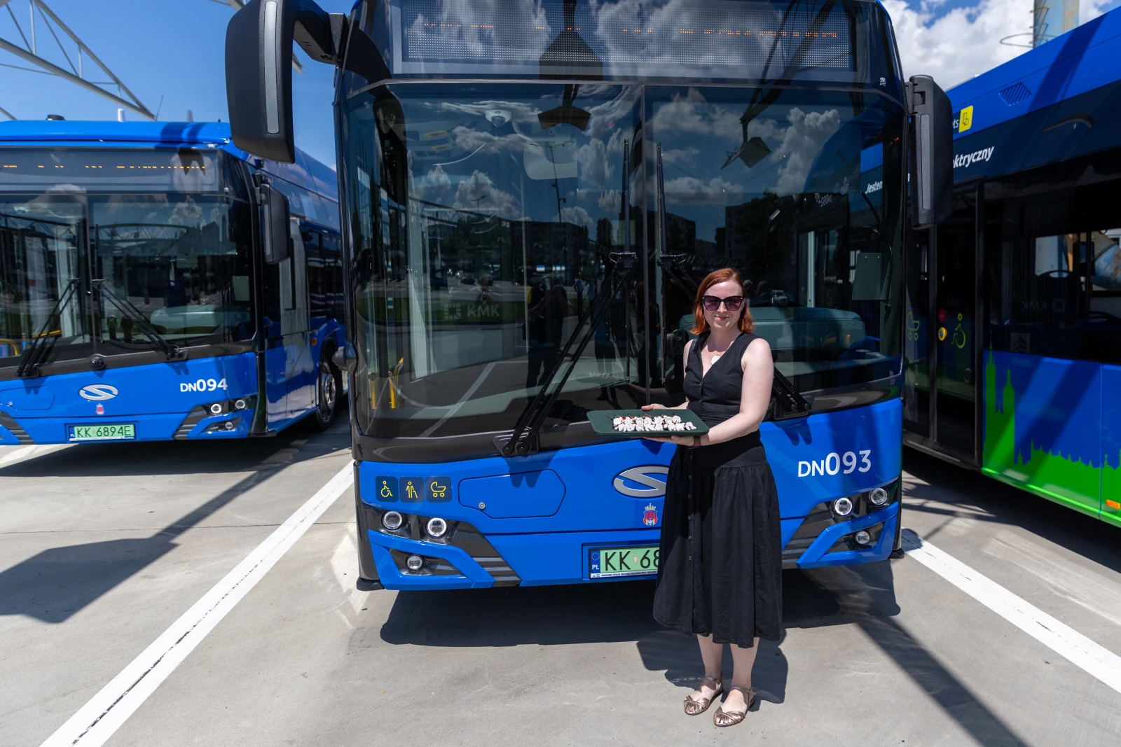 Kobieta w czarnej sukience trzyma tort przed niebieskim autobusem.  Autor: Bogusław Świerzowski