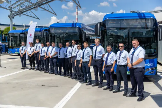 Grupa pracowników w uniformach stojąca obok nowoczesnych autobusów.