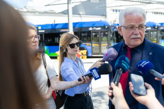 Mężczyzna udziela wywiadu, otoczony przez dziennikarzy z mikrofonami.