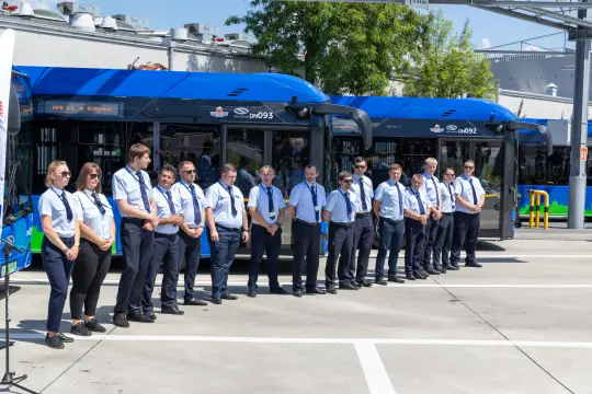 Grupa pracowników w uniformach stojąca obok nowoczesnych autobusów.