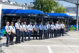 Grupa pracowników w uniformach stojąca obok nowoczesnych autobusów.