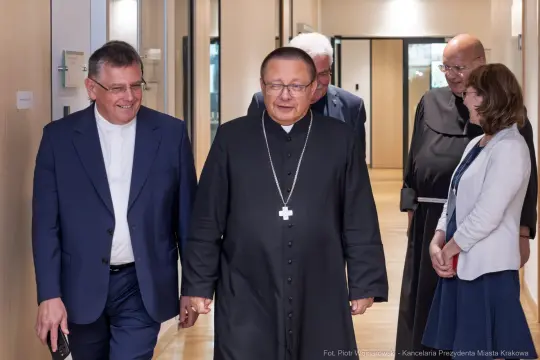 Grupa osób w formalnych strojach idzie korytarzem.