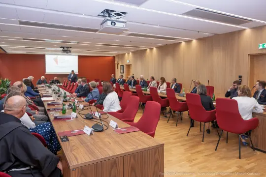 Spotkanie w sali konferencyjnej z uczestnikami przy stole, prezentacja na ekranie.