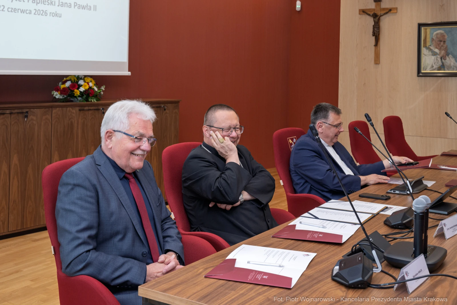 Trzech mężczyzn siedzących przy stole w sali konferencyjnej, z krzyżem na ścianie.  Autor: Piotr Wojnarowski