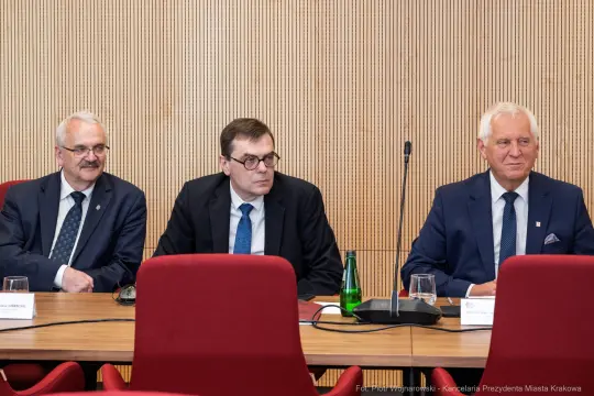 Trzech mężczyzn siedzących przy stole w sali konferencyjnej.