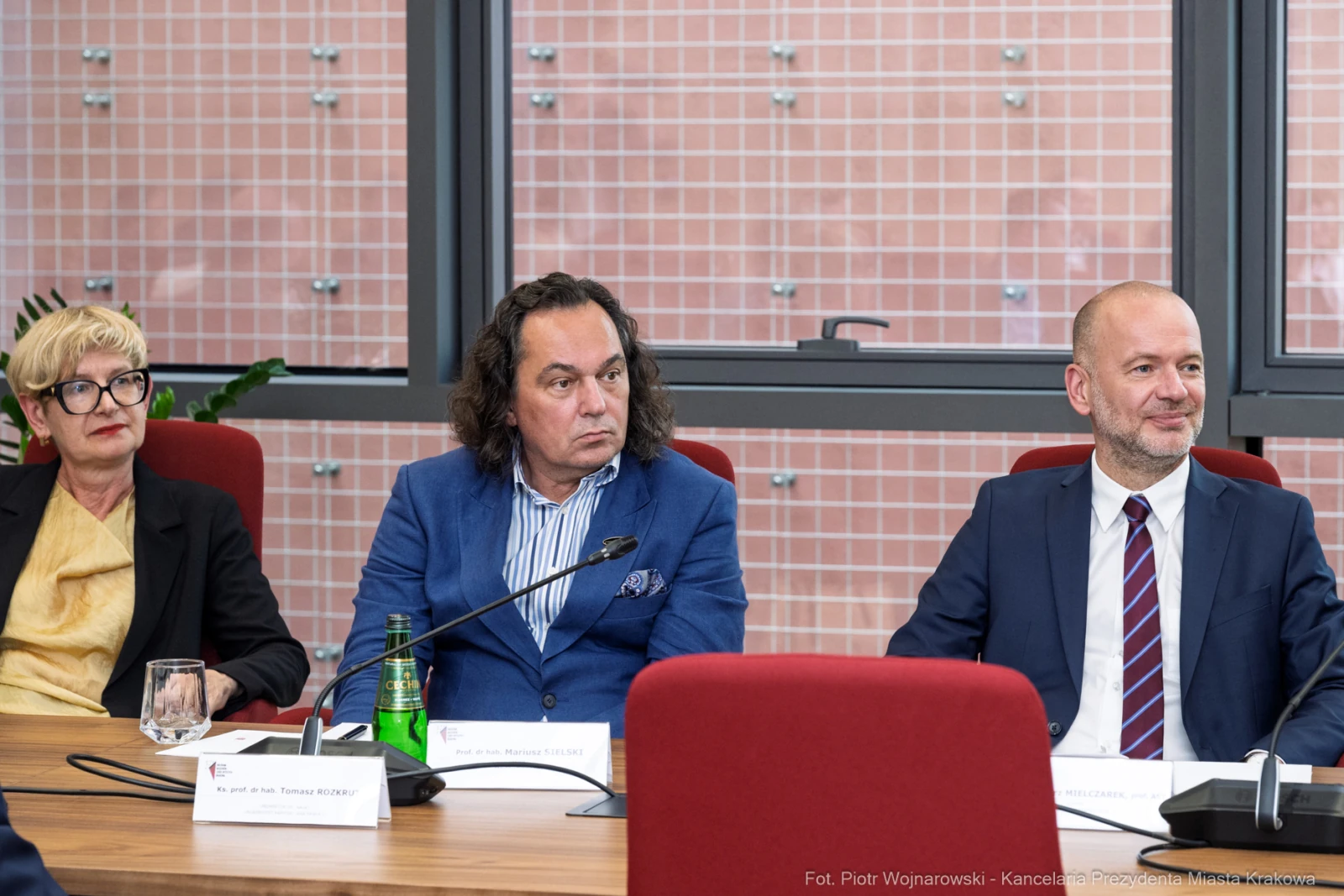 Trzy osoby siedzą przy stole, rozmawiając, w tle okna i roślinność.  Autor: Piotr Wojnarowski
