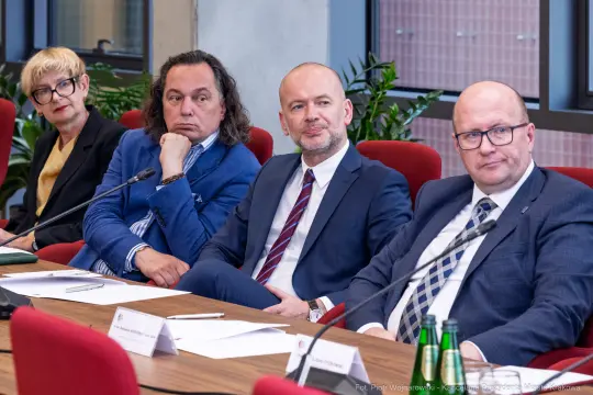 Czterech mężczyzn i jedna kobieta siedzą przy stole w sali konferencyjnej.