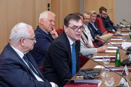 Spotkanie grupy mężczyzn przy stole, dyskusja w formalnym otoczeniu.