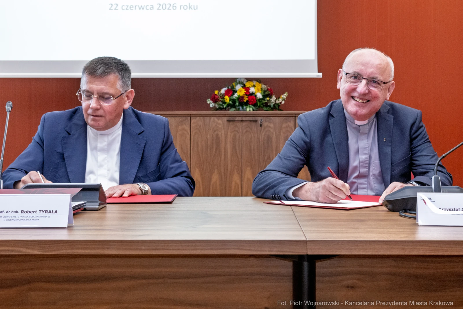 Dwóch mężczyzn przy stole podpisuje dokumenty, w tle kwiaty.  Autor: Piotr Wojnarowski