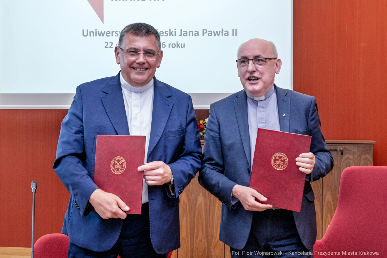 Dwaj mężczyźni w garniturach trzymają dokumenty, uśmiechając się podczas ceremonii podpisania umowy.  Autor: Piotr Wojnarowski