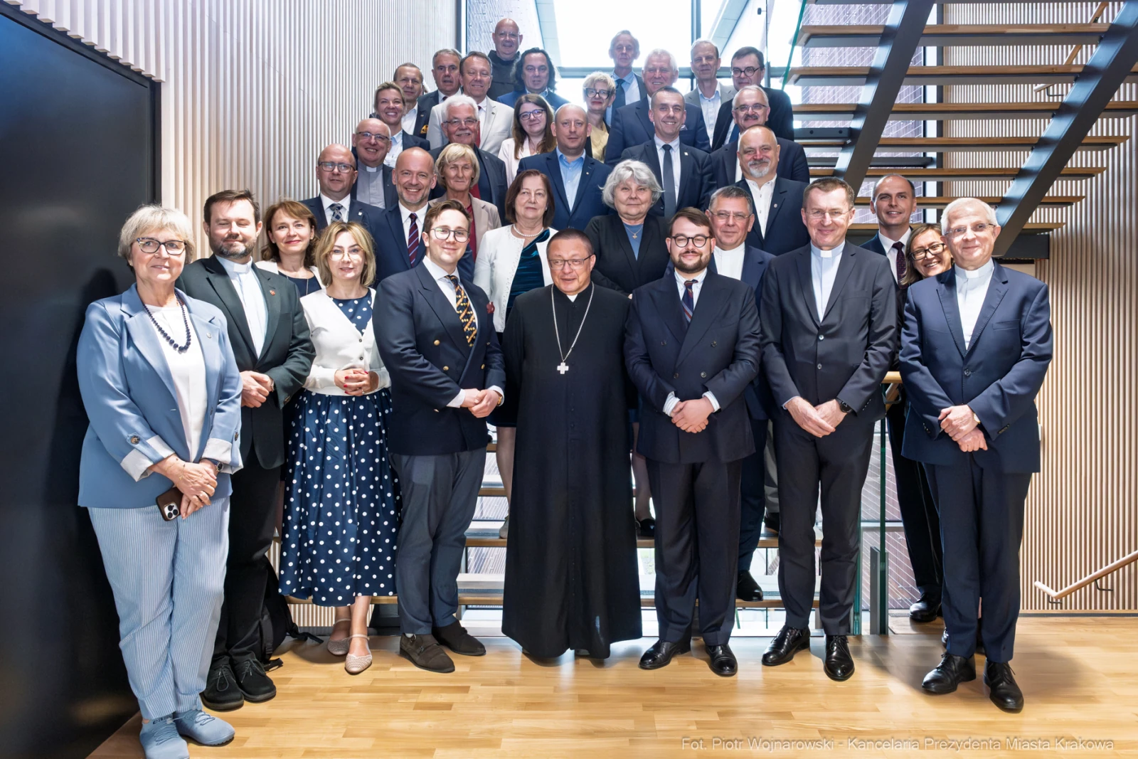 Grupa osób w formalnych strojach, pozująca na schodach w nowoczesnym wnętrzu.  Autor: Piotr Wojnarowski