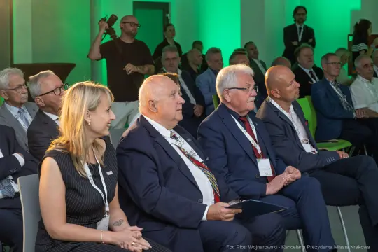 Grupa osób siedzących na konferencji, z zainteresowaniem słuchających prelegenta.