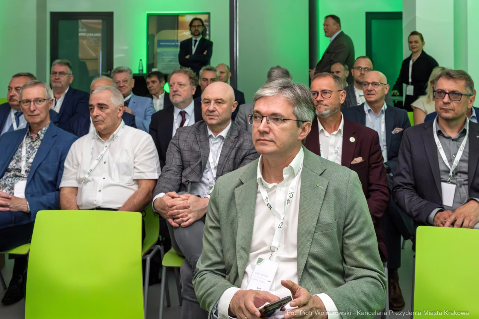 Grupa mężczyzn w garniturach siedzących na zielonych krzesłach podczas wydarzenia.  Autor: Piotr Wojnarowski