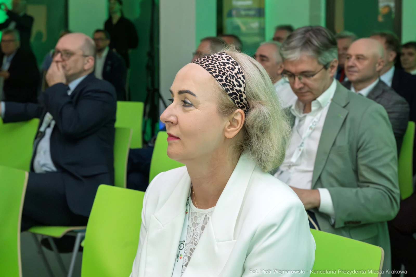 Kobieta w białej marynarce z opaską na głowie siedzi na konferencji, w tle mężczyźni w garniturach.  Autor: Piotr Wojnarowski