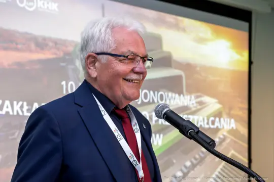 Mężczyzna w garniturze uśmiecha się podczas przemówienia na konferencji.