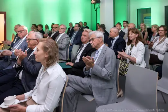 Grupa ludzi w formalnych strojach, klaskających podczas wydarzenia.