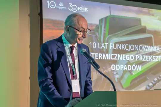 Mężczyzna przemawia na tle prezentacji dotyczącej 10-lecia funkcjonowania termicznego przekształcania odpadów.