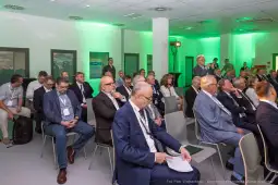 Grupa osób siedzących na konferencji, w tle zielone oświetlenie.