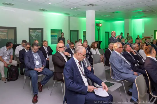 Grupa osób siedzących na konferencji, w tle zielone oświetlenie.
