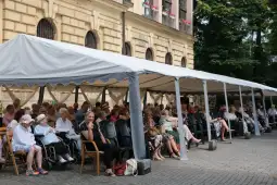Grupa starszych osób siedzących pod namiotem w parku.